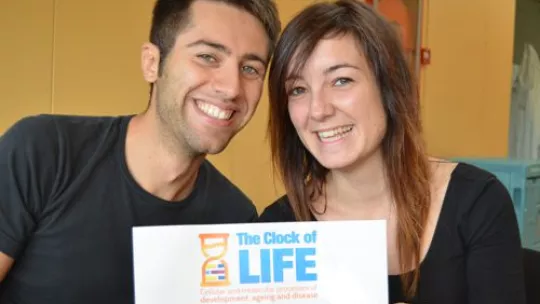 Simone Pieretti and Jessica Vitos, two of the organizers, with the poster of the 3rd IRB PhD Symposium (Photo L.T. Barone)